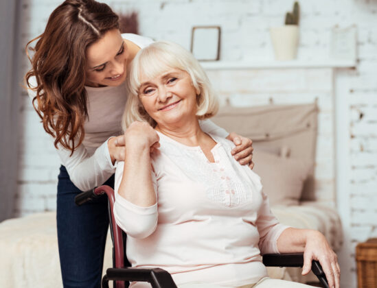 My dear. Pleasant elderly woman smiling and sitting in the wheelchair while her loving granddaughter taking care of her